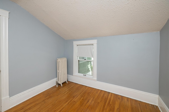 additional living space with lofted ceiling, radiator, a textured ceiling, wood finished floors, and baseboards