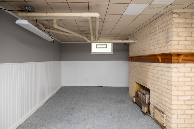 below grade area with a wainscoted wall, a brick fireplace, and a paneled ceiling