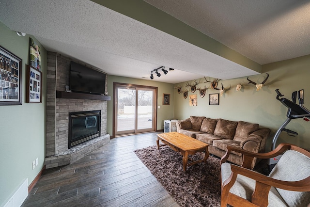 living area with baseboards, wood finished floors, a textured ceiling, a brick fireplace, and track lighting