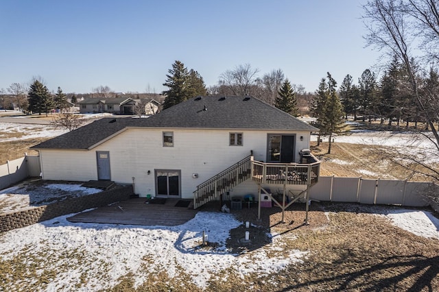 snow covered property featuring a fenced backyard, stairway, a deck, and roof with shingles