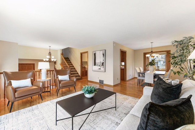 living room featuring stairway, baseboards, visible vents, light wood finished floors, and an inviting chandelier