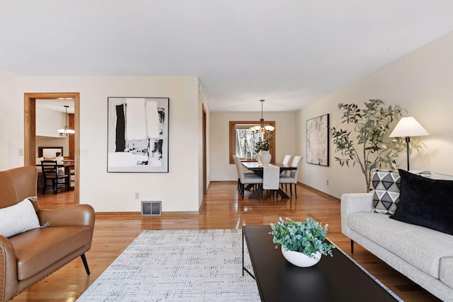 living room featuring a notable chandelier, visible vents, light wood-style flooring, and baseboards