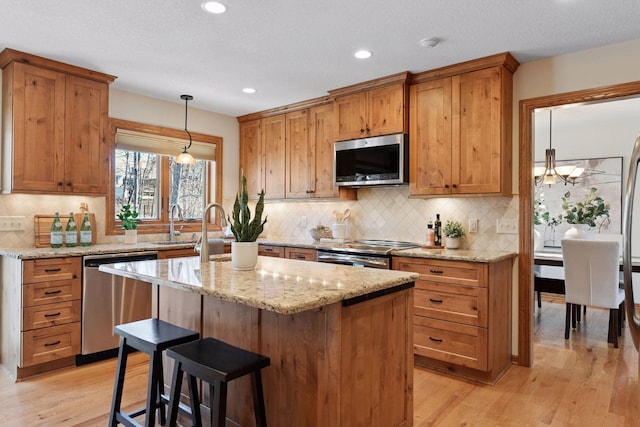 kitchen featuring light wood finished floors, stainless steel appliances, light stone counters, and a kitchen island with sink