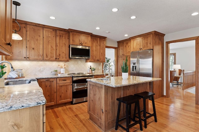 kitchen with light stone counters, a kitchen island with sink, a sink, appliances with stainless steel finishes, and light wood-type flooring