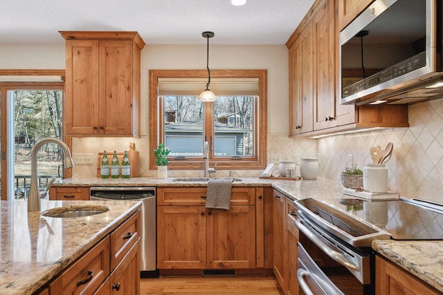 kitchen featuring light stone counters, light wood-type flooring, appliances with stainless steel finishes, and a sink