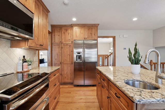 kitchen featuring a sink, stainless steel appliances, light wood-style floors, brown cabinets, and a center island