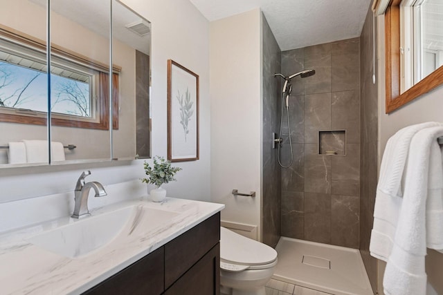 bathroom with visible vents, toilet, a textured ceiling, a tile shower, and vanity