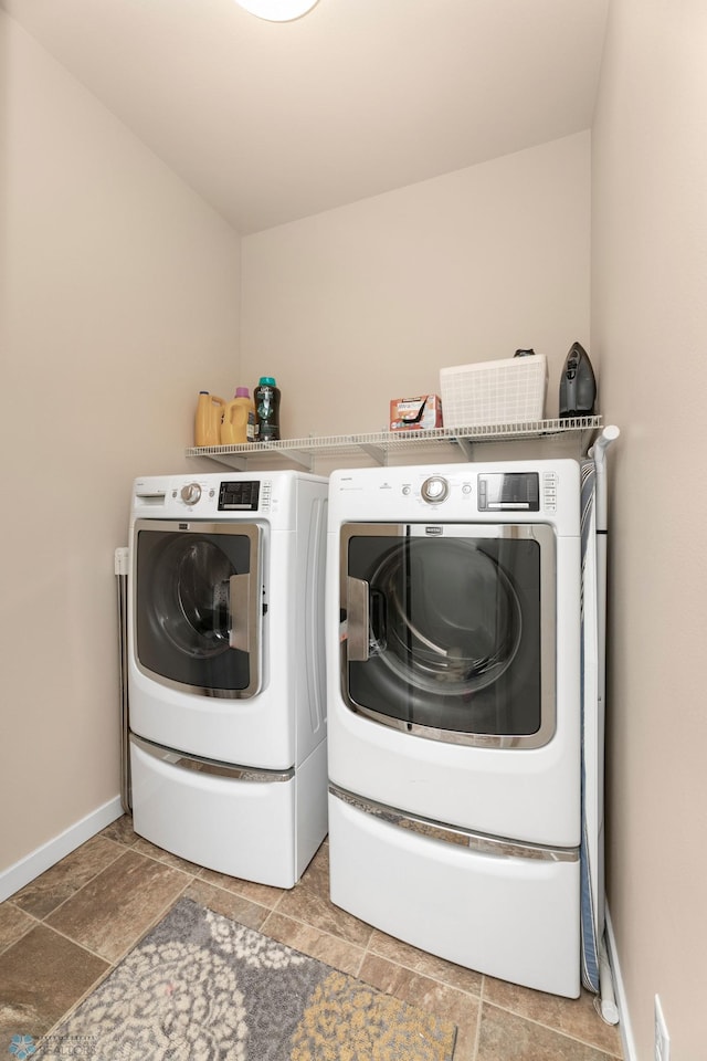 clothes washing area featuring laundry area, stone finish floor, independent washer and dryer, and baseboards