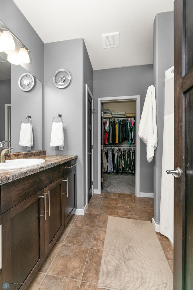 bathroom featuring visible vents, vanity, baseboards, and a spacious closet