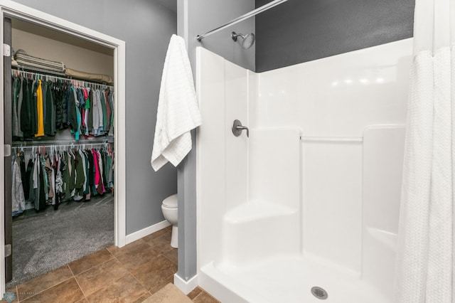 bathroom with a spacious closet, a shower stall, toilet, and baseboards