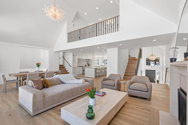 living area featuring recessed lighting, a fireplace, stairs, light wood finished floors, and an inviting chandelier