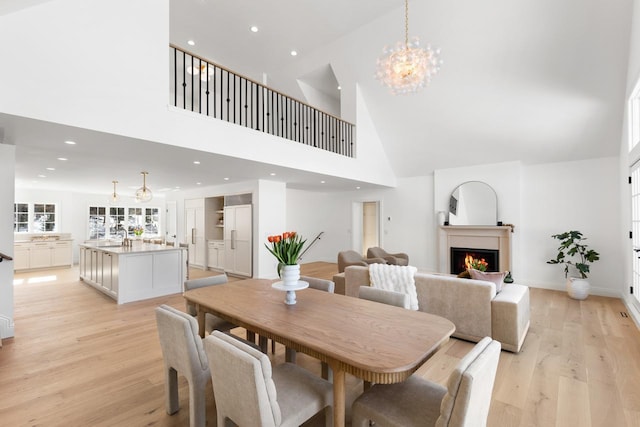 dining area featuring light wood-type flooring, a warm lit fireplace, a notable chandelier, and recessed lighting