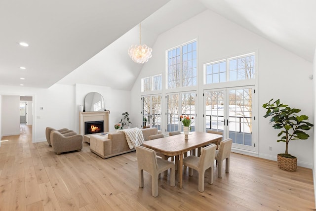 dining room featuring light wood finished floors, a lit fireplace, high vaulted ceiling, and baseboards