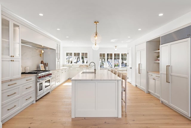 kitchen featuring glass insert cabinets, double oven range, a sink, and light wood finished floors