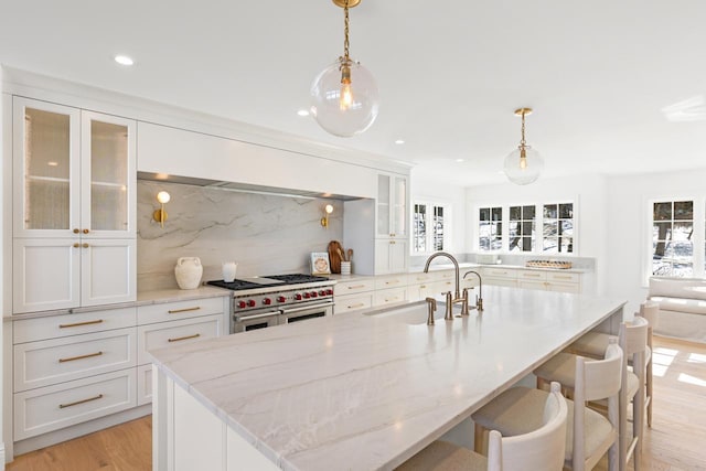 kitchen featuring white cabinets, double oven range, a sink, and light wood-style flooring