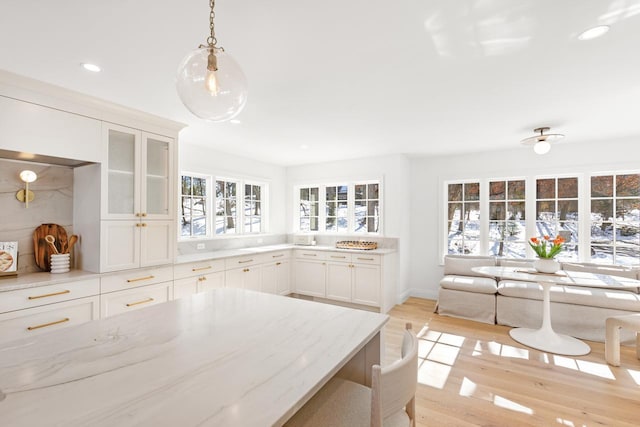 kitchen with light stone counters, hanging light fixtures, light wood-style flooring, glass insert cabinets, and white cabinets