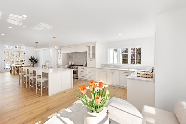 kitchen with light wood-style flooring, glass insert cabinets, high end range, and white cabinets