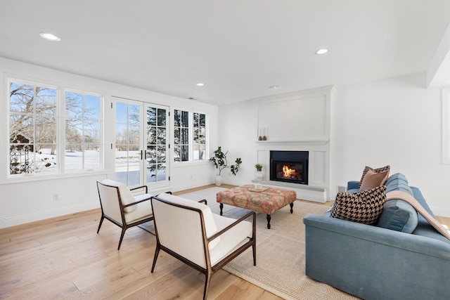 living area featuring light wood-style floors, a glass covered fireplace, baseboards, and recessed lighting