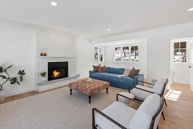 living area featuring light wood finished floors, recessed lighting, and a glass covered fireplace