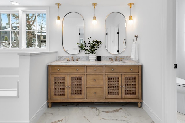 bathroom featuring toilet, marble finish floor, double vanity, and a sink