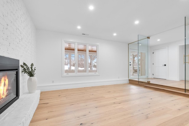 unfurnished living room featuring light wood finished floors, visible vents, baseboards, a stone fireplace, and recessed lighting