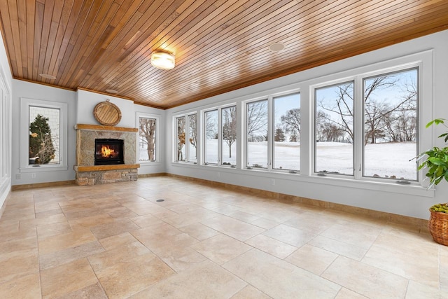 unfurnished living room with wooden ceiling, baseboards, ornamental molding, and a stone fireplace