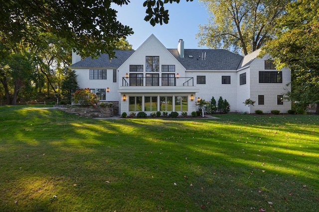 back of property with a balcony, a chimney, a lawn, and roof with shingles