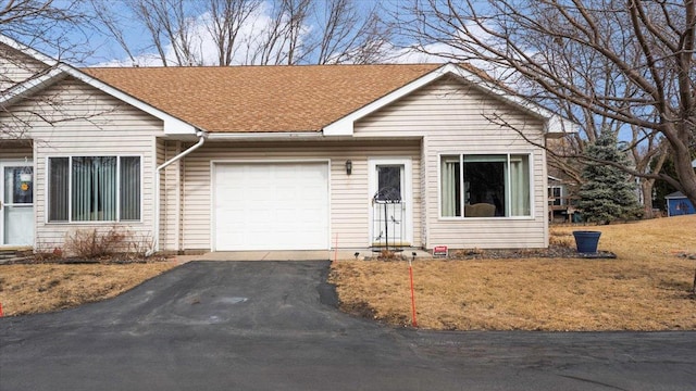 ranch-style house featuring aphalt driveway, roof with shingles, an attached garage, and a front lawn