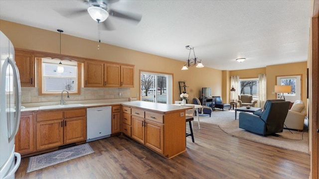 kitchen with a peninsula, white appliances, a sink, open floor plan, and light countertops