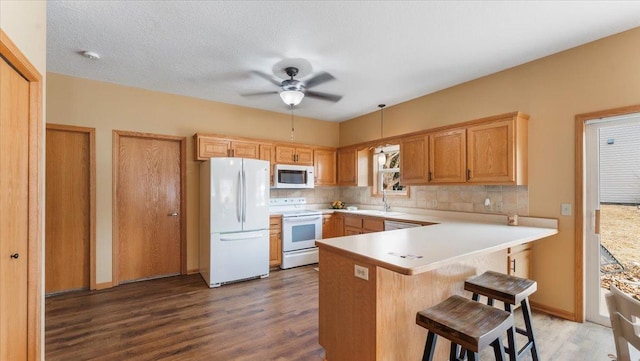 kitchen with white appliances, tasteful backsplash, a kitchen breakfast bar, wood finished floors, and a peninsula