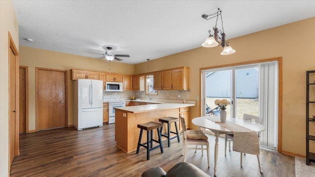 kitchen featuring decorative light fixtures, tasteful backsplash, light countertops, dark wood-type flooring, and white appliances