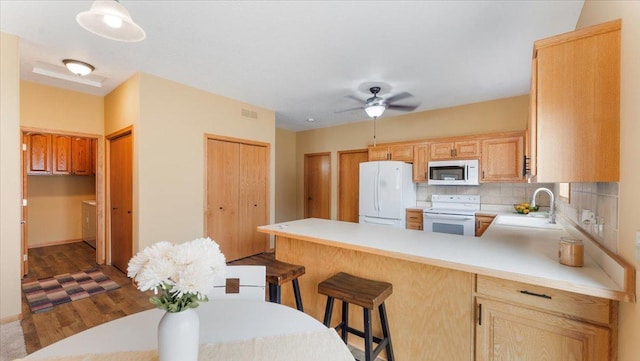 kitchen featuring white appliances, decorative backsplash, a peninsula, light countertops, and a sink