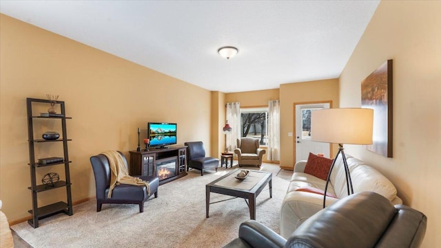 living room featuring a glass covered fireplace, light colored carpet, and baseboards