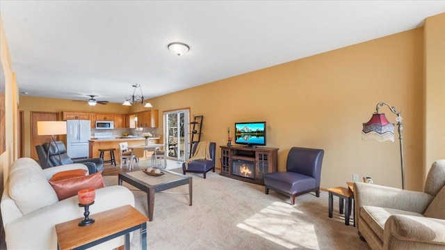 living room featuring a ceiling fan, light colored carpet, and a lit fireplace