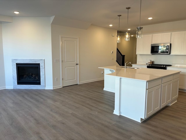 kitchen with a center island with sink, stainless steel microwave, dark wood-style flooring, a sink, and recessed lighting