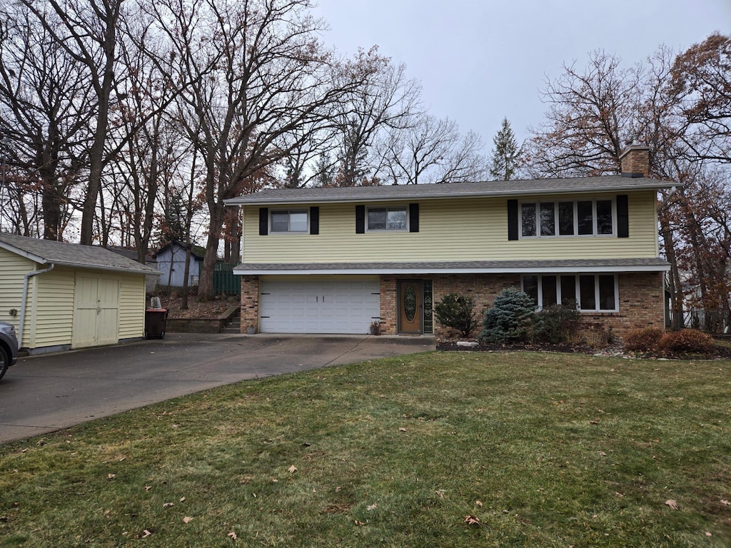 traditional-style house with brick siding, a chimney, an attached garage, driveway, and a front lawn