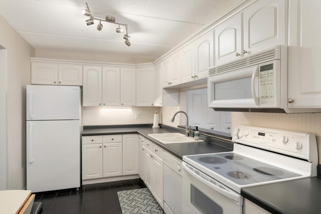 kitchen with dark tile patterned floors, white appliances, dark countertops, and a sink