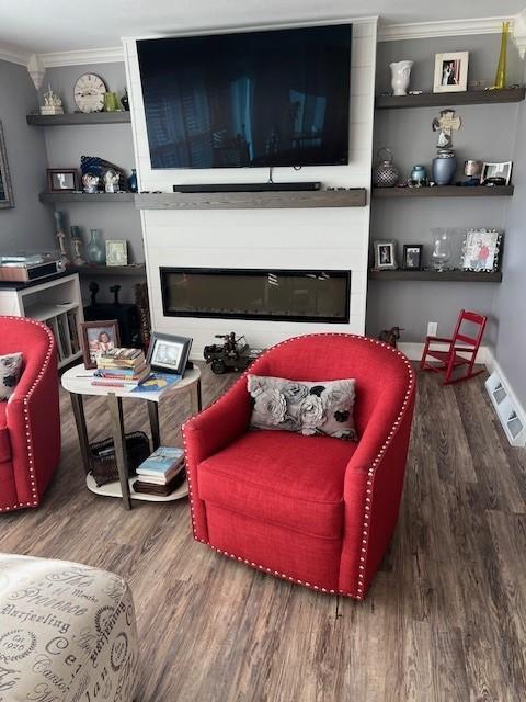 living area with ornamental molding, visible vents, a fireplace, and wood finished floors