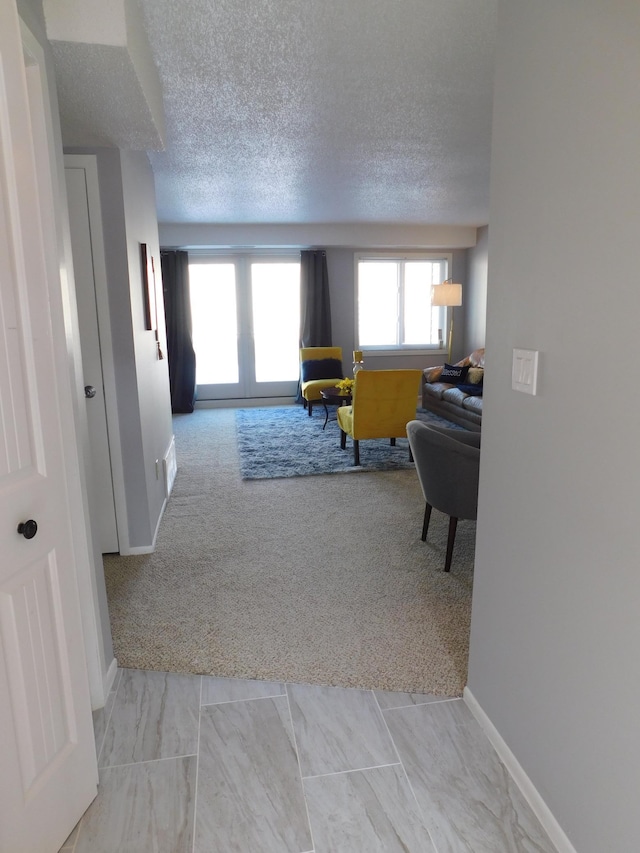 living area with carpet, baseboards, a textured ceiling, and french doors