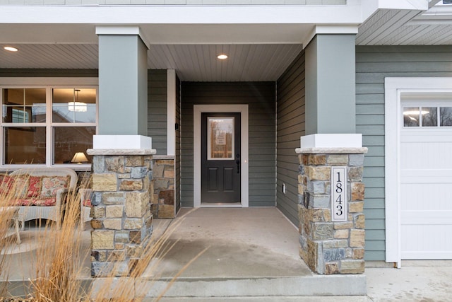 view of exterior entry with a garage, stone siding, and covered porch