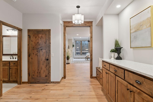 hall with recessed lighting, light wood-type flooring, a sink, and baseboards