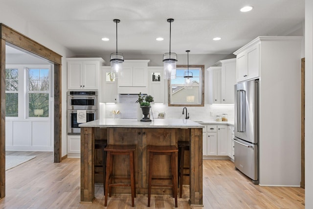 kitchen featuring a breakfast bar, a kitchen island, light wood-style floors, white cabinets, and appliances with stainless steel finishes