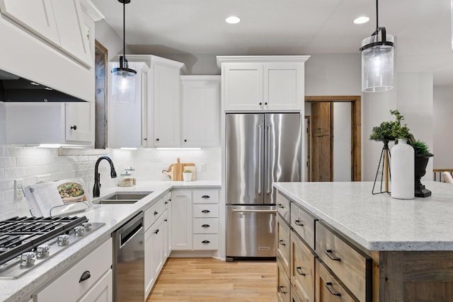 kitchen with appliances with stainless steel finishes, light wood-type flooring, a sink, and tasteful backsplash