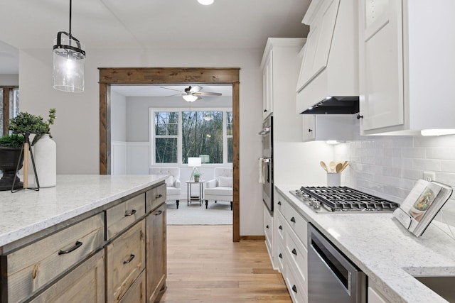 kitchen featuring light stone counters, premium range hood, appliances with stainless steel finishes, decorative backsplash, and light wood finished floors