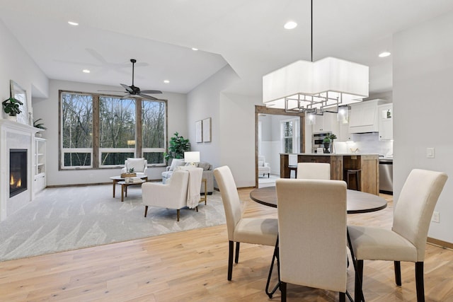 dining area featuring light wood-style floors, recessed lighting, ceiling fan with notable chandelier, and a glass covered fireplace