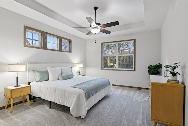 bedroom featuring light carpet, baseboards, a raised ceiling, and a ceiling fan