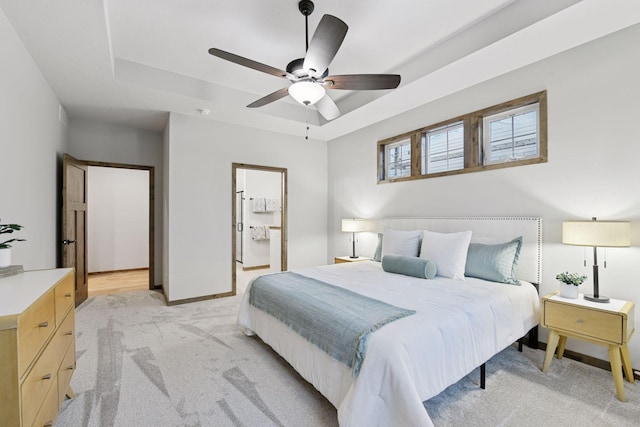 bedroom with a raised ceiling, light colored carpet, ceiling fan, ensuite bath, and baseboards