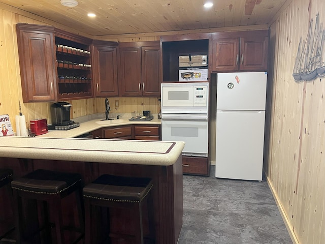 kitchen with light countertops, wood ceiling, a sink, wooden walls, and white appliances