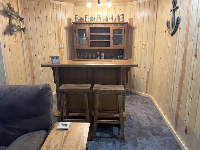 bar with a dry bar, wood walls, and baseboards