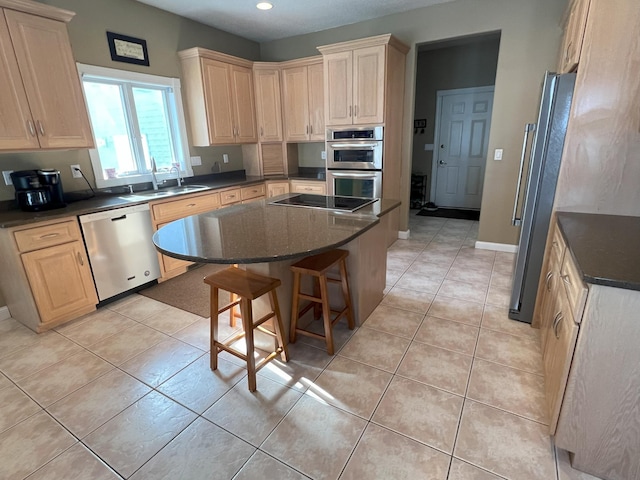 kitchen with light tile patterned flooring, a sink, appliances with stainless steel finishes, a center island, and dark countertops